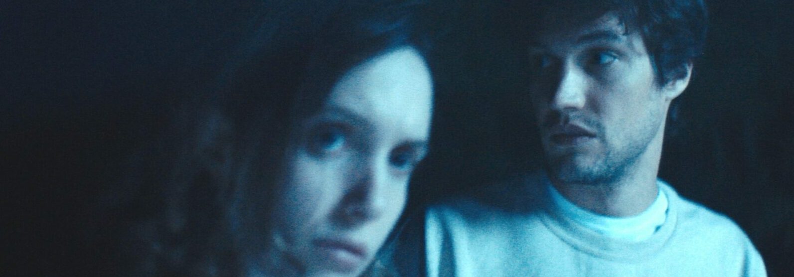 A still from Robert McMahon's film showing two people in close up bathed in a blue light with black bacgkround.