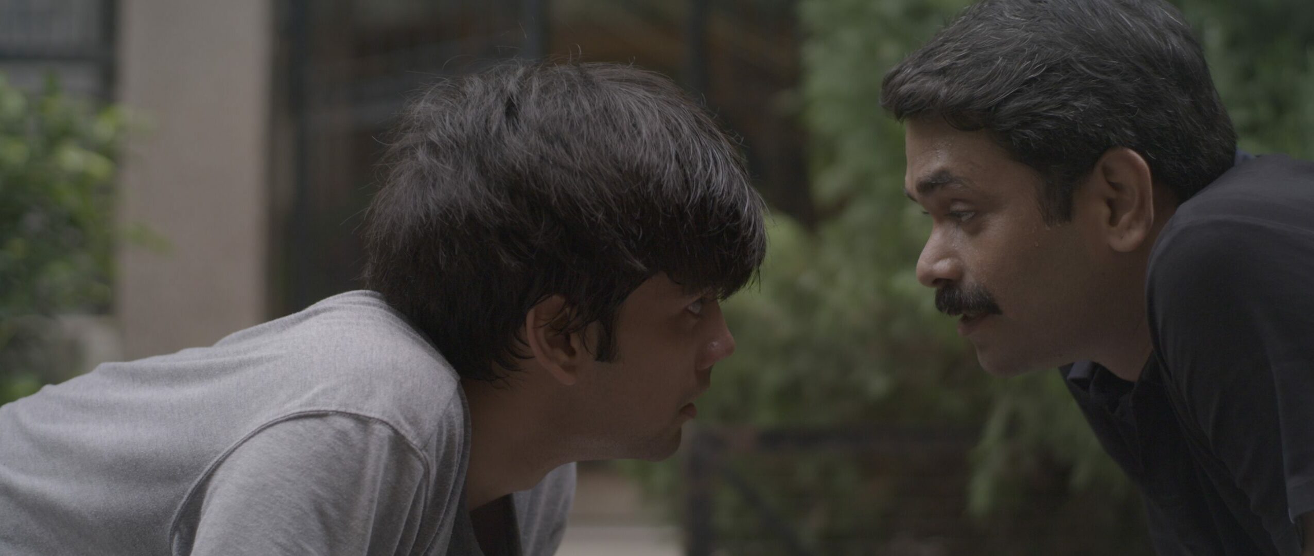 Still image from Arnav's Film Subah shows a father and son looking intensely at each other in front of green foliage.