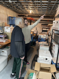 behind the scenes photo of Kenny standing next to Ray as Kenny points to a shelf of boxes.