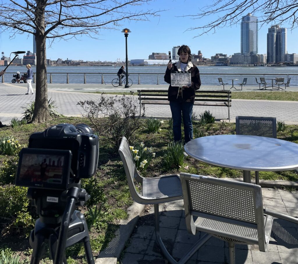 a camera is setup on a tripod outside while a crew member prepares to slate