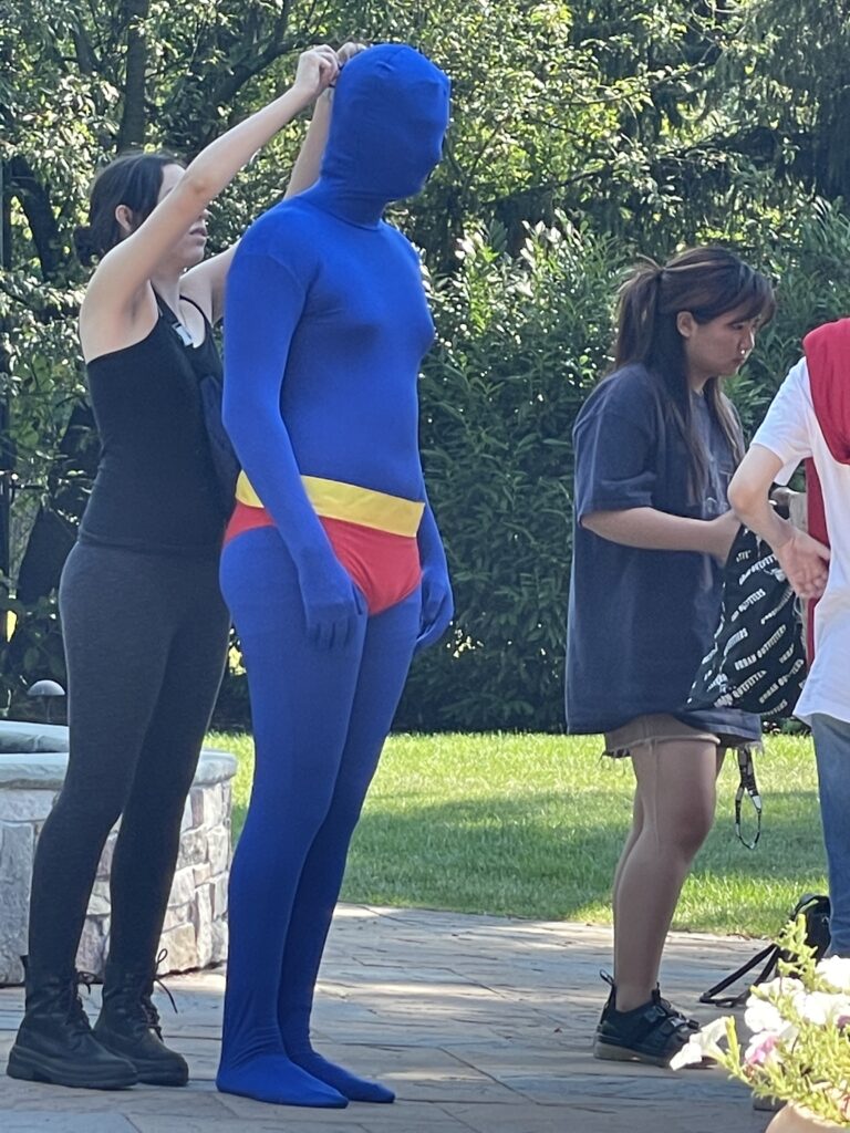 an actor wearing a full body blue suit being adjusted by an assistant