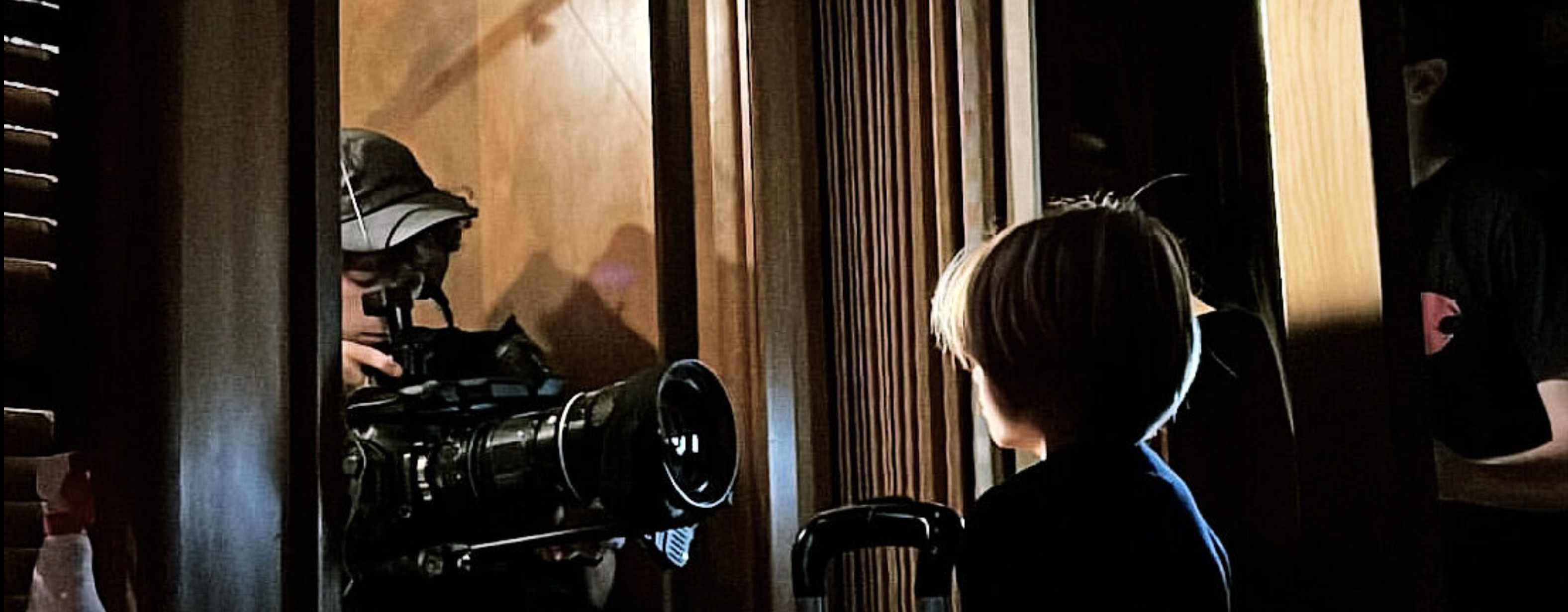 a child actor standing in a dark room, a cinematographer holding a camera in front of the child actor