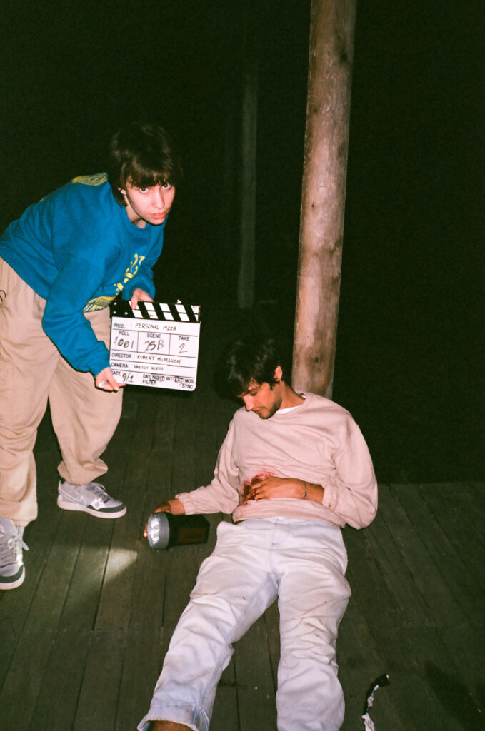 Behind the scenes photo of Roberts film showing a crew member with a clapboard and an actor laying on the ground ready to shoot their scene.