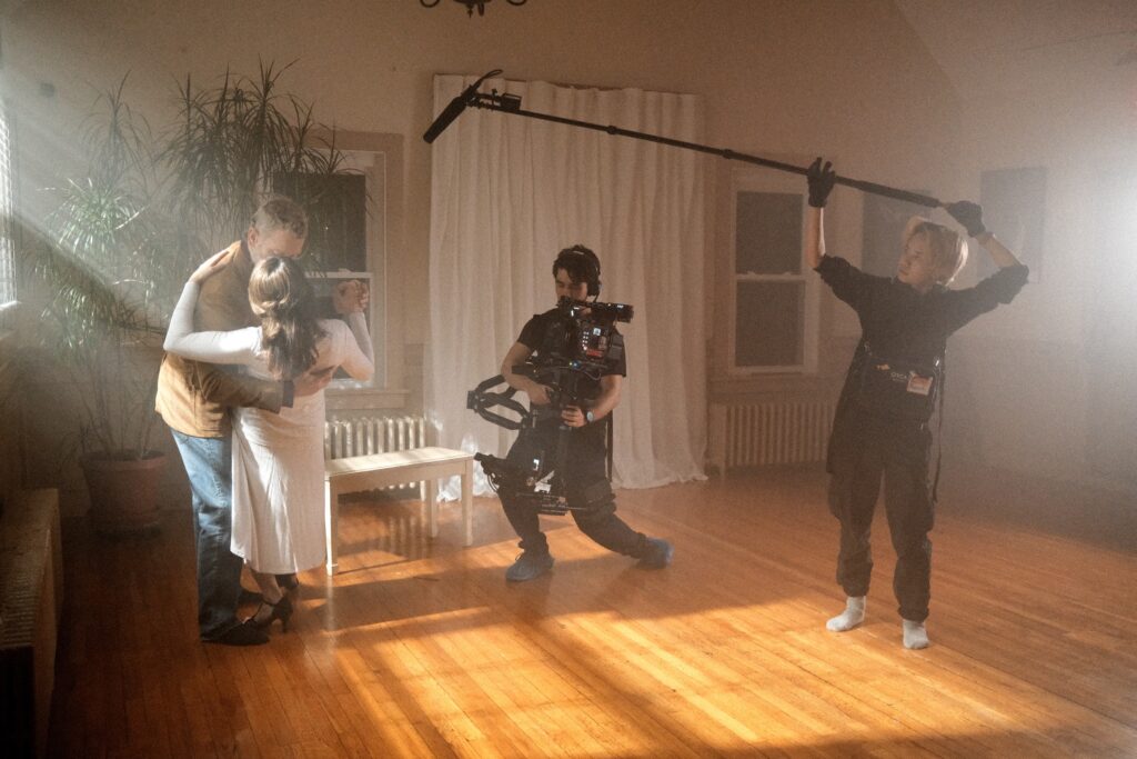 behind the scenes photo from roberts shoot showing a sound person holding a boom pole with the mic and the camera person filming two actors.