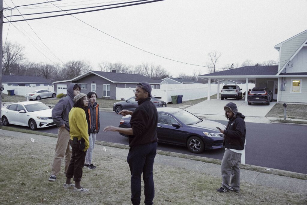 behind the scenes photo from Khalil's film that shows a group of people standing outside on a lawn by the street preparing for a shot.