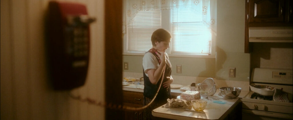 An actor from the film speaks on a landline phone while in a kitchen.