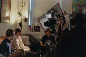 On set of You Will Find Love. The actors sit on a sofa going through a scene, and on the other side is the crew watching the camera and working on sound.