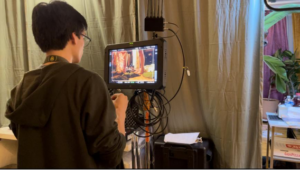 The 1st AC has his back to the image, as he works in front of the monitor, pulling focus on a scene.