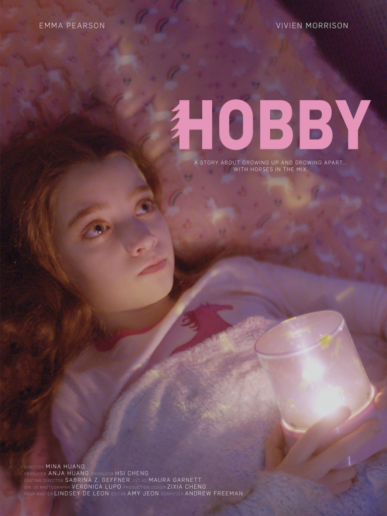 Poster for Mina's film Hobby. Shows a young girl laying on pink bedsheets and holding a candle with the title in big pink letters next to her face.