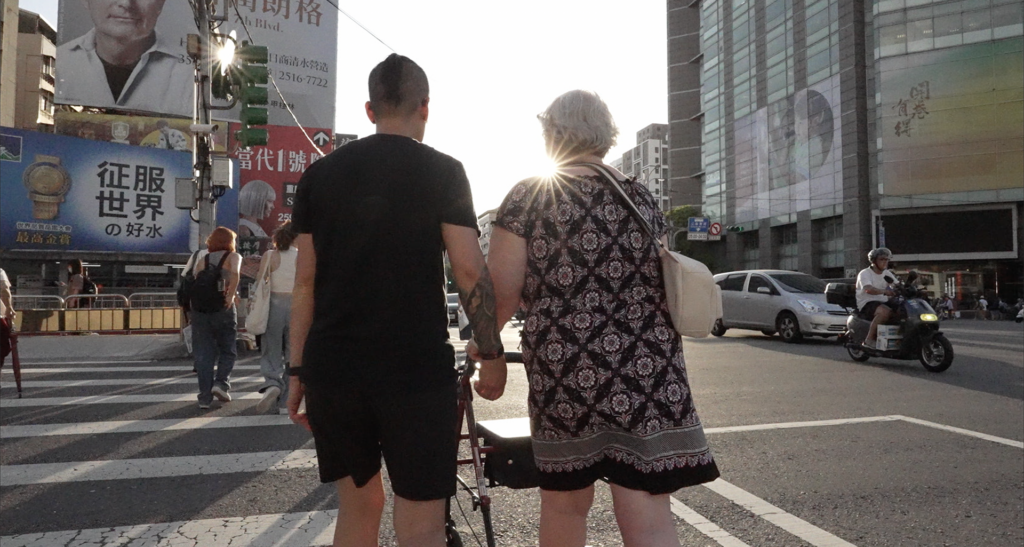 A still from the documentary “Find Me” the subject Kuo and her adoptive mother Mary holding hands while crossing the busy street in Taipei.