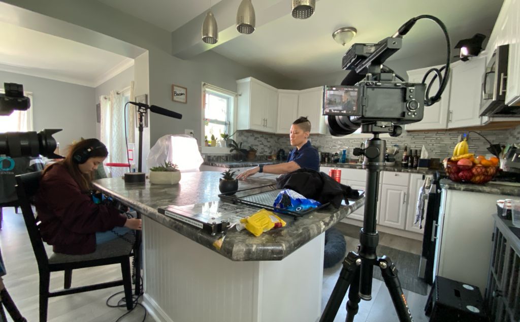 A camera and a boom mic is pointing at the interviewee Kuo, who is sitting in the middle of the kitchen, filming in process