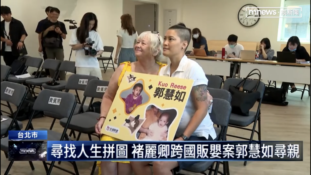 A screenshot of a news report from Taiwan, “Looking at Kuo and Mary holding a sign with her name Kuo Reese, her Chinese name, and photo of her as a baby. They sit at the front roll of the chairs at a press conference, 