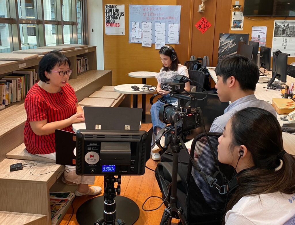 Two filmmakers and a reporter on the right side, a women in red shirt is talking in front of the camera