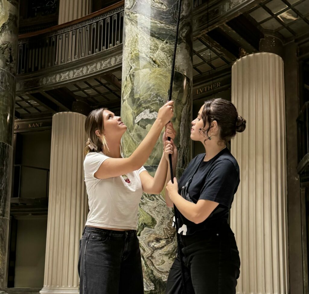 Two girls hold a cord, keeping the frame hung in the ceiling from falling.