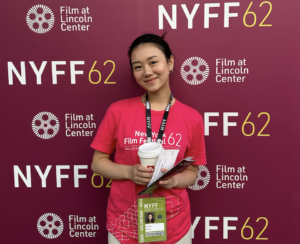 Student Shuran Zhang, volunteering at the festival, standing in front of NYFF's backdrop.