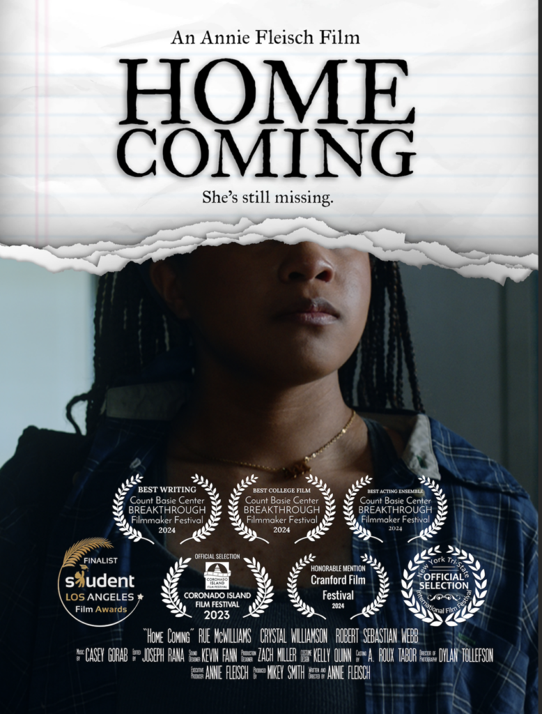 Poster for the film Home Coming. The words “An Annie Fleisch Film”, the title “Home Coming”, and the tagline, “She’s still missing,” comprise the top half of the poster, which is designed as black text against a notebook paper background. The bottom half is a dark photo of a young woman’s face and chest, “ripped off” just above her nose. Credits in small white text are displayed at the very bottom of the poster, and seven film festival laurels decorate the area above them. 