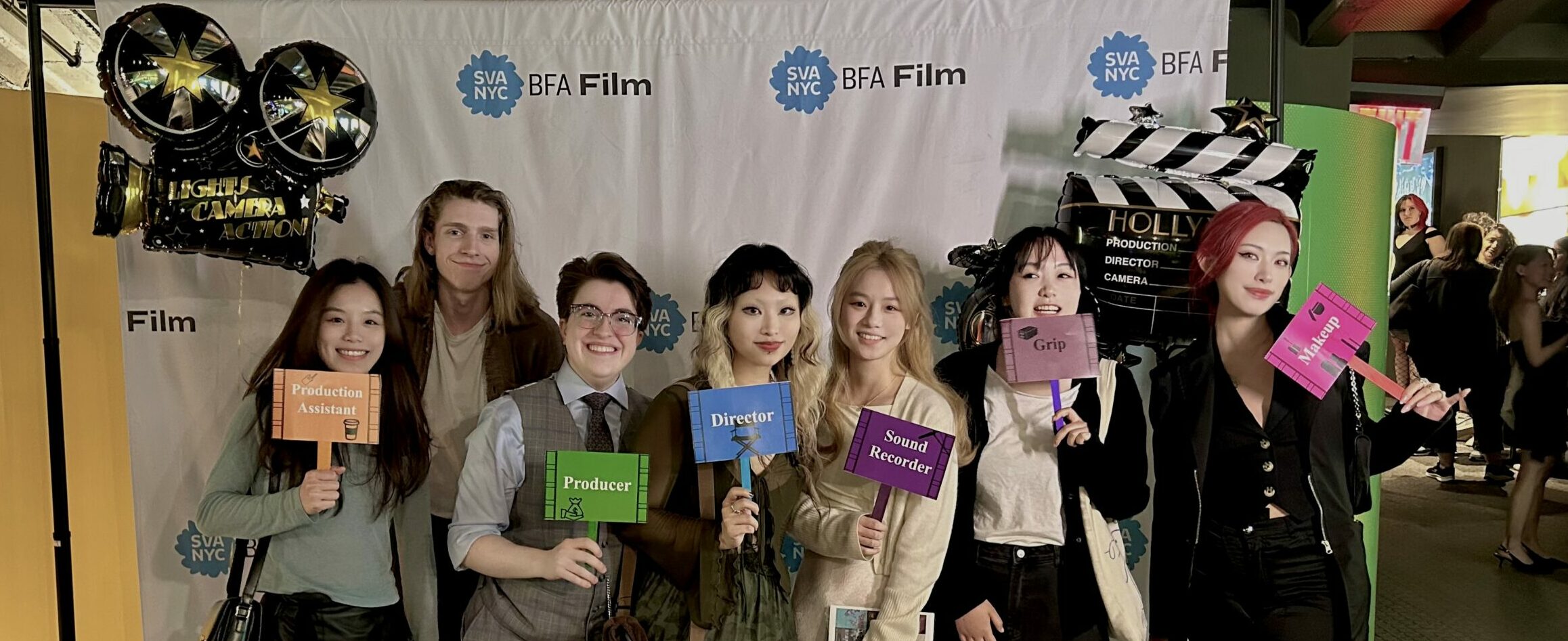 The crew of Lucky Shot is in front of an SVA BFA Film banner, dressed up. They smile to the camera and hold plaques that display their work on set. Director Zixia (Jessica) Cheng is in the middle.