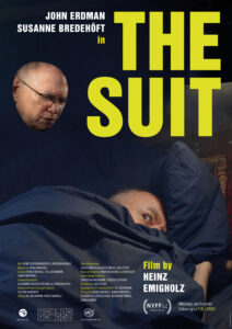 Poster for the film The Suit. Shows a person laying down while an older man stares down at them from behind.