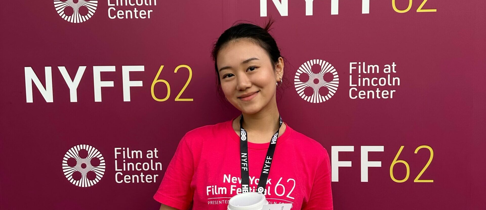 Student Shuran Zhang, volunteering at the festival, standing in front of NYFF's backdrop.